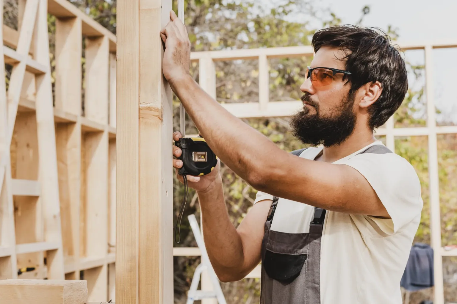 Carpenter using a tape measure with printed plans on the bench
